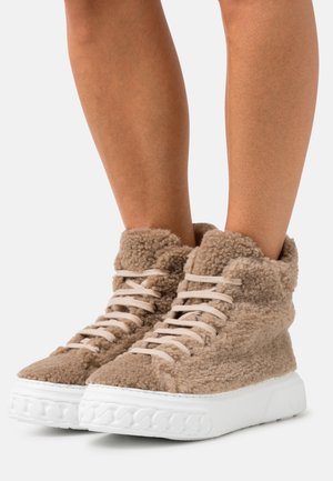 Høje sneakers i beige blødt materiale med hvide gummisåler og matchende snørebånd, der har et tekstureret, blødt design.