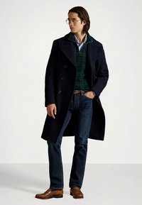 Marineblå ull peacoat med store slag, grønn rutete genser, blå jeans og brune loafers. Klart, teksturert stoff og skreddersydd passform.