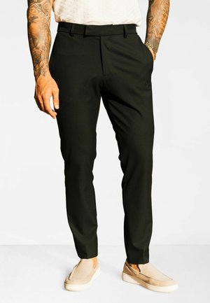 Pantaloni negri croiți, cu o croială strâmtă, având o textură fină și buzunare frontale. Purtați cu pantofi bej slip-on.