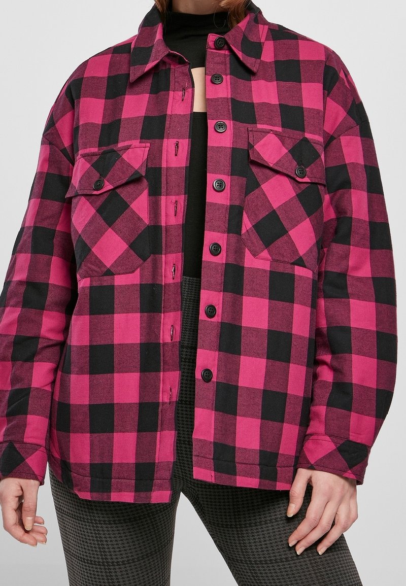 Camisa de cuadros en rosa y negro con cuello, dos bolsillos en el pecho y mangas largas. Fabricada en una suave tela tejida.