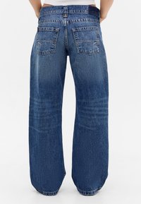 Wijdvallende blauwe denim jeans met een hoge taille, grote achterzakken en subtiele wassingdetails op de stof.
