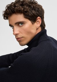 Dunkelblaues geripptes Rollkragensweatshirt mit hohem Kragen und strukturiertem Muster, in taillierter Silhouette und mit langen Ärmeln.