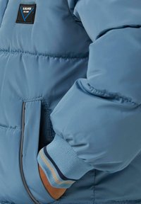 Lichtblauwe gewatteerde jas met ribgebreide manchetten. Voorzien van een logo patch en zakdetails, met een soepele, glanzende stofstructuur.