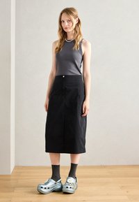 Haut sans manches gris, jupe noire au genou, et sabots bleus avec des embellissements floraux, assortis à des chaussettes grises. Textures lisses et design simple.