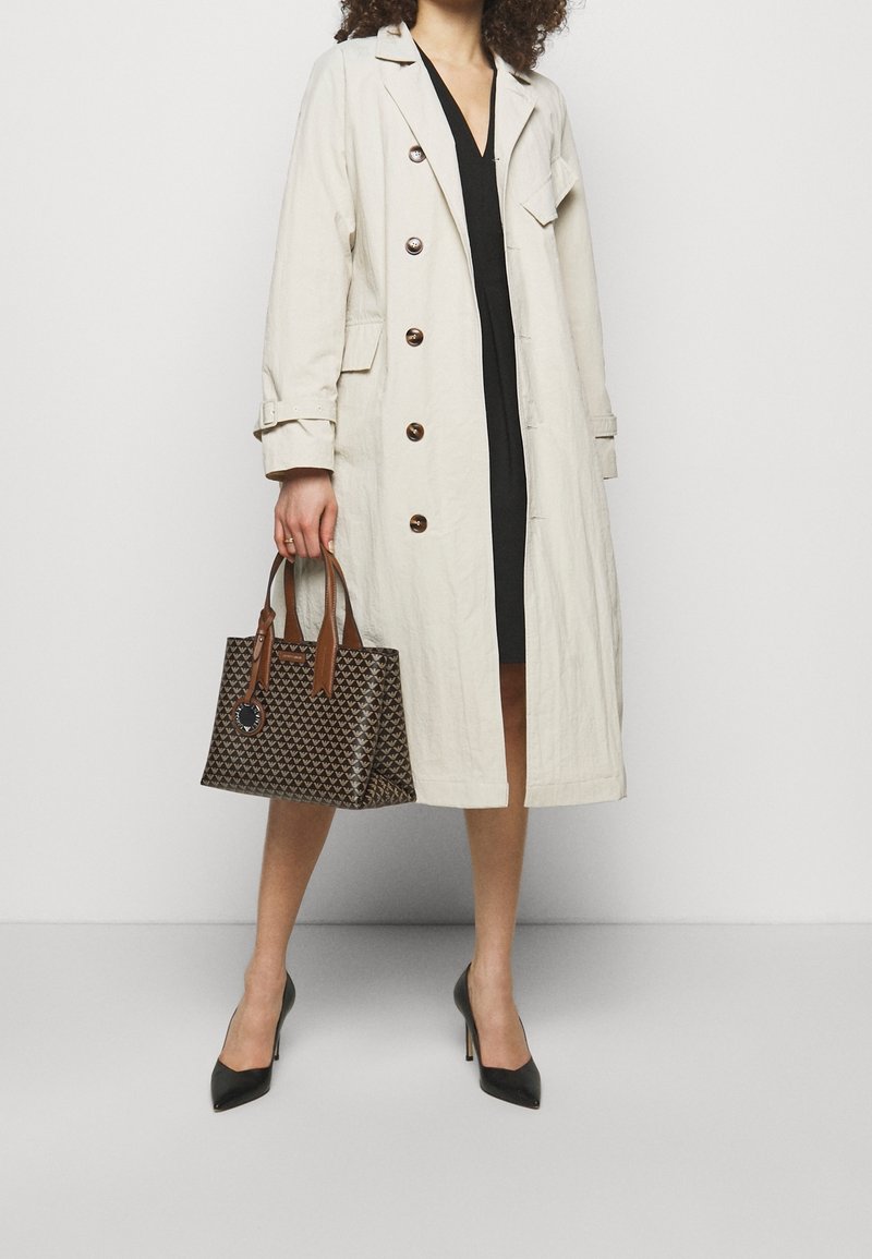 Bežový trench coat s knoflíky, černé šaty a hnědá vzorovaná kabelka s koženými uchy. Černé vysoké podpatky. Hladké textury.