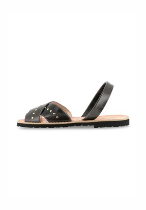 Black leather sandals with crisscross straps, gold studs, and a back sling. The sole is flat and made of textured rubber.