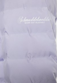 Hele lavendlivärvi puhvjakke, millel on tikitud disain, sile ja läikiva kangaga ning valge logo tekstiga: "Schmuddelwedda, Wenn dat pladdert."