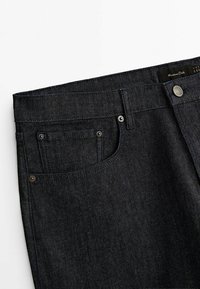 Mörka denimjeans med en mjuk textur, femfickorsdesign, metallknappar och diskret sömnad. Har en etikett vid midjebandet.