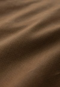 Tissu brun texturé avec un motif de grille fine, présenté en gros plan avec une lumière douce et des plis délicats.