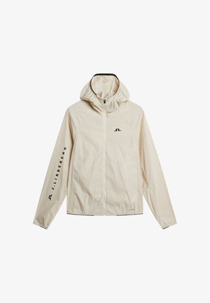 Veste beige légère à capuche avec fermeture éclair complète à l'avant, petit logo noir sur la poitrine et texte "J. Lindeberg" le long de la manche gauche.