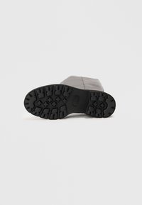 Semelle extérieure en caoutchouc noir d'une botte avec des motifs de semelle profonds. Matériau supérieur marron lisse avec des détails de couture visibles.
