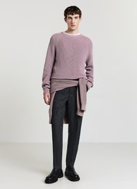 Maglione lilla chiaro a coste indossato sopra una camicia scura a fantasia, abbinato a pantaloni scuri e stivali neri robusti.