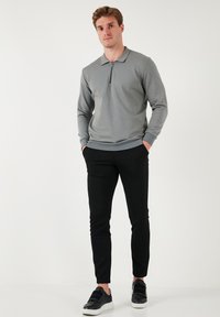 Šedý pulóver so zipsom a golierom, dlhými rukávmi a rebrovaným lemom, skombinovaný s čiernymi slim-fit nohavicami a čiernymi teniskami. Jednoduchý dizajn.