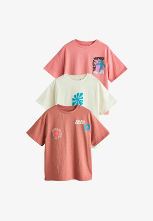 Kolme lyhythihaista rentoa t-paitaa korallinpunaisena, luonnonvalkoisena ja roosana, joissa on sinivalkoisia graafisia kuvioita ja tekstiä rintakehässä.