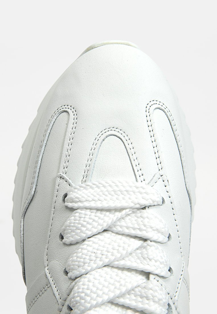 Weiße Ledersneaker mit strukturiertem Obermaterial, runder Form und traditionellem Schnürdesign, ausgestattet mit dicken weißen Schnürsenkeln und seitlichen Nahtdetails.