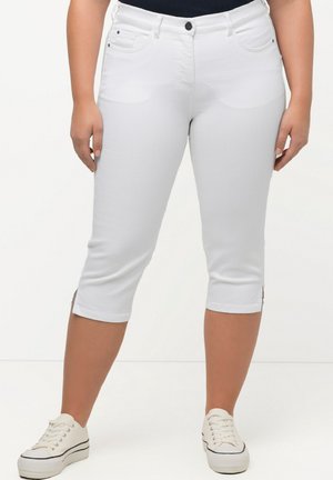 Pantalones capri blancos en denim elástico, con cierre de botón en el frente, cinco bolsillos y aberturas en el dobladillo, combinados con zapatillas de lona blancas.