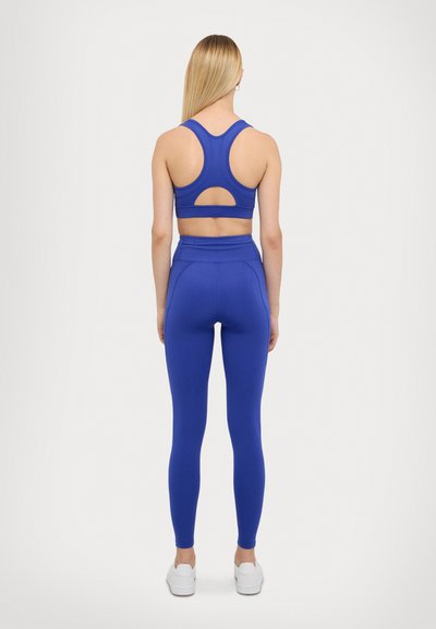 Blue sports bra with racerback design and cutout detail, paired with high-waisted blue leggings. Smooth, stretchy fabric, minimal accents.
