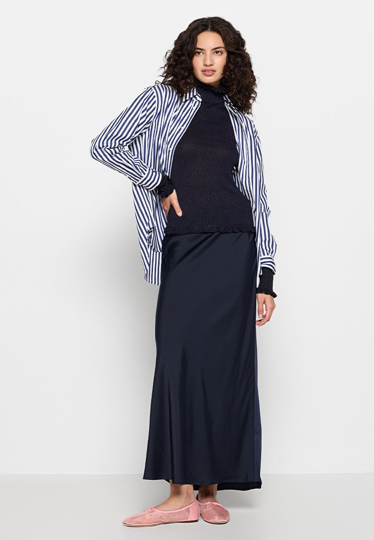 Veste à rayures bleues et blanches, associée à une jupe bleu marine et des ballerines roses. Pull texturé sombre en dessous. Silhouette simple et élégante.