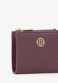 Portafoglio in pelle color bordeaux con superficie strutturata, caratterizzato da un emblema con logo dorato e chiusura a zip. Design compatto con bordi puliti.