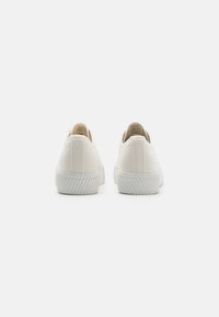 Canvas slip-on shoes in off-white with textured surface, reinforced heel, and rubber sole featuring vertical grooves for traction.