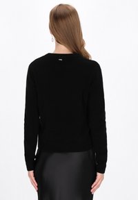 Maglione nero con maniche lunghe, scollatura rotonda e orlo a coste. Tessuto morbido con una piccola etichetta sul retro. La silhouette cade appena sopra la vita.