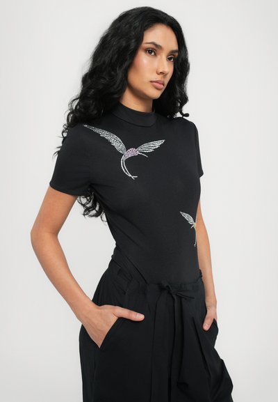 Black fitted bodysuit with a high neckline and rhinestone bird design on the chest. Soft texture, short sleeves, paired with loose black pants.