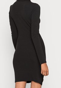 Robe noire à manches longues en tissu côtelé, avec une silhouette ajustée et un ourlet légèrement arrondi. Aucun motif ni accent visible.