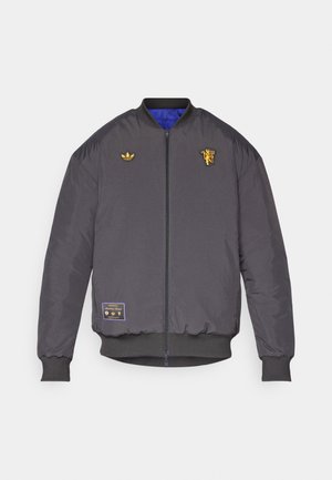 Veste bomber charbon avec un intérieur bleu. Présente des logos brodés en or et une fermeture zippée. Manches et ourlet côtelés. Tissu résistant.
