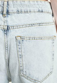 Vaaleansinisiä farkkushortseja, joissa on korkea vyötärö, tavallinen takatasku ja näkyvät ompeluakkentit. Kankaassa on haalistunut tekstuuri.