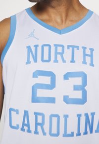 Maillot de basket blanc avec des touches bleu clair. Présente "NORTH" et "CAROLINA" brodés en bleu clair, avec le numéro "23" en dessous. Comprend un logo Jordan.
