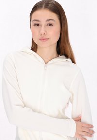 Valkoinen vetskarihuppari, joka on valmistettu pehmeästä kankaasta; siinä on huppu, pitkät hihat ja etuvetoketju. Sileä pinta, jossa on vähäistä yksityiskohtaisuutta.