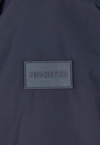Marineblauwe stof met een gladde textuur, voorzien van een rechthoekige rubberen patch met de opgeperste tekst "HECHTER" in hoofdletters.