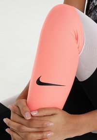 Leggings Nike en corail rose, avec un logo noir. Le tissu est lisse avec un mélange de couleurs et de textures, ajusté autour des jambes.
