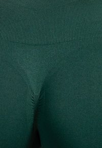 Grüne gestrickte Leggings mit einer gerippten Textur, ausgestattet mit einem hohen Taillenbund und einem dreieckigen Keil-Design in der Mitte.