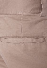Tessuto beige con una sottile trama diagonale, dotato di una tasca a filetto sul retro, evidenziata da cuciture ordinate.