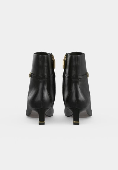 Par de botines negros de cuero con tacones bajos, cremalleras doradas visibles y correas con hebillas vistos desde atrás sobre un fondo blanco.