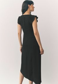 Robe noire avec des manches courtes à volants, un buste ajusté et un ourlet légèrement asymétrique. Tissu lisse avec une fermeture éclair cachée dans le dos.