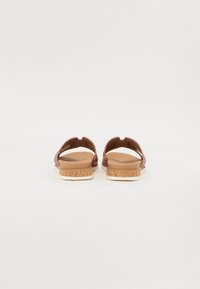 Brune sandaler i syntetisk materiale med korkstrukturert såle, åpen bak, og dekorativt utskjæringsdesign.