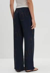 Pantalon large en tissu bleu marine avec une surface texturée et des motifs abstraits marron. Doté d'une taille élastique pour plus de confort.