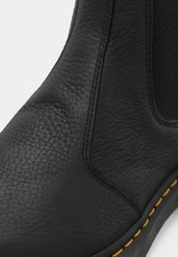 Zwarte, gestructureerde leren Chelsea boot met elastische zijpanel en gele steekdetails op de rand van de zool.