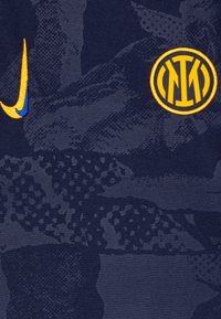 Marinblått tyg med en strukturerad mönster som har en gul Nike-logotyp och en rund, gul Inter Milan-emblem. Slät och sportig design.