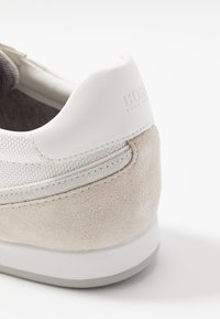 Tenisky s horní částí z lehké šedé semišové kůže a bílé kožené části, texturované akcenty a měkkým bílým podpatkem se zvýrazněným logem.