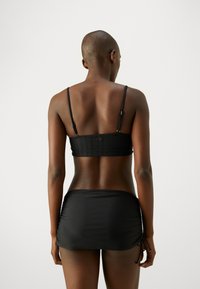 Schwarzer Bikini-Oberteil mit verstellbaren Trägern und strukturierter Stoff, kombiniert mit einem passenden Bade-Rock mit Zugbandakzenten.