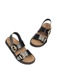 Las sandalias de cuero negro cuentan con dos correas anchas con hebillas doradas, una plantilla de un tono marrón claro y una suela negra con tachuelas doradas a lo largo del borde.