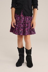 Černý žebrovaný cardigan přes sukni s květinovým potiskem v růžové a fialové barvě s volány, doplněnou černými semišovými kozačkami se stříbrnými cvočky a bočním zipem.