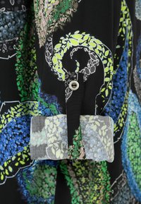 Black fabric sleeve with multicolored floral paisley pattern, green and blue details, rolled cuff, and a single button fastening strap.