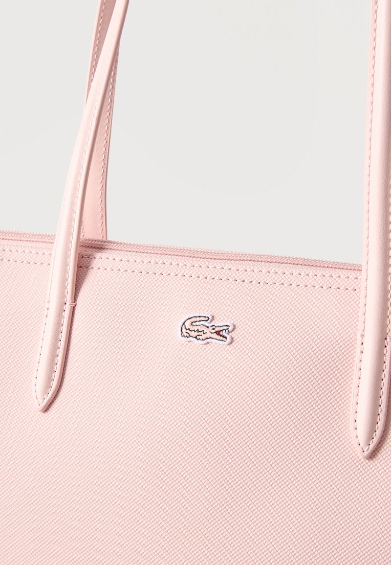 Borsa tote rosa chiaro texturizzata con doppi manici e piccolo logo ricamato del coccodrillo Lacoste vicino al bordo superiore.