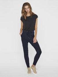 Black short-sleeve top with a relaxed fit, paired with navy tapered pants featuring an elastic drawstring waist. Beige sneakers complete the outfit.