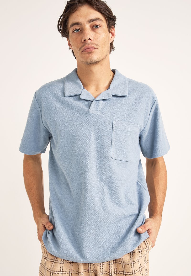 Polo de manga corta en azul claro, hecho de tejido texturizado, con un cuello y un bolsillo de parche en el lado izquierdo del pecho.
