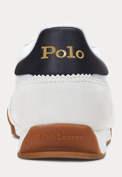 Λευκό πίσω μέρος αθλητικού παπουτσιού με μαύρη γλωττίδα στη φτέρνα που φέρει χρυσό κείμενο "Polo" και καφέ σόλα με ανάγλυφη επιγραφή "Ralph Lauren".